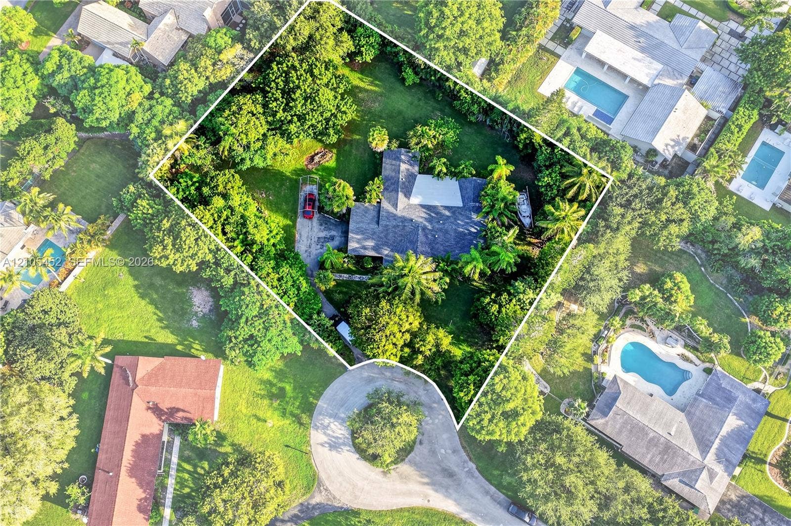 Aerial view of a residential property featuring a sprawling lot, dense mature canopy, paved driveway, and established landscape foliage