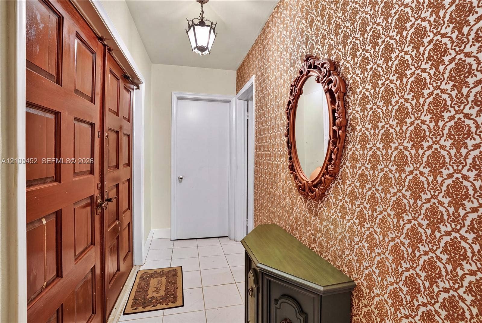 Entryway featuring double wood-paneled doors, ceramic tile flooring, and patterned wallcovering