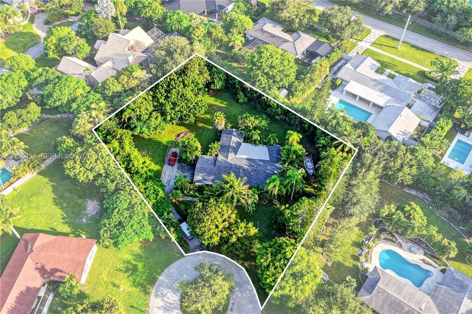 Aerial perspective of a sprawling property featuring mature canopy trees, expansive lawn space, and a multi-section roofline