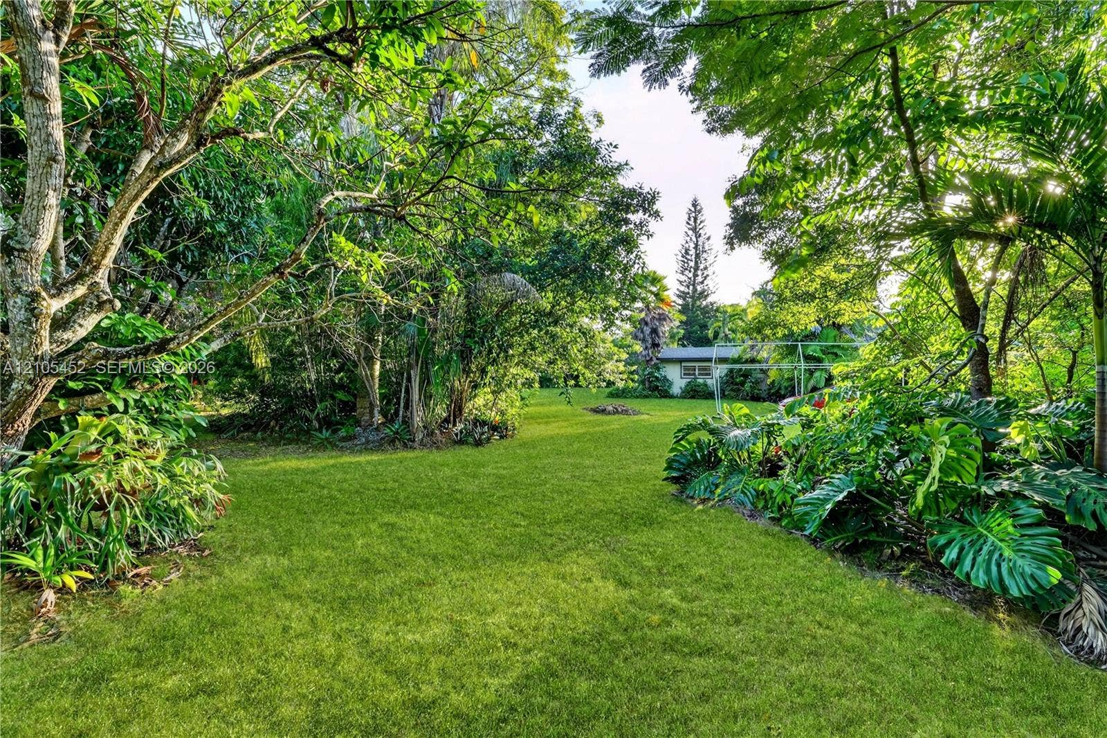 Expansive backyard featuring a lush grass lawn, established shade trees, and mature tropical foliage