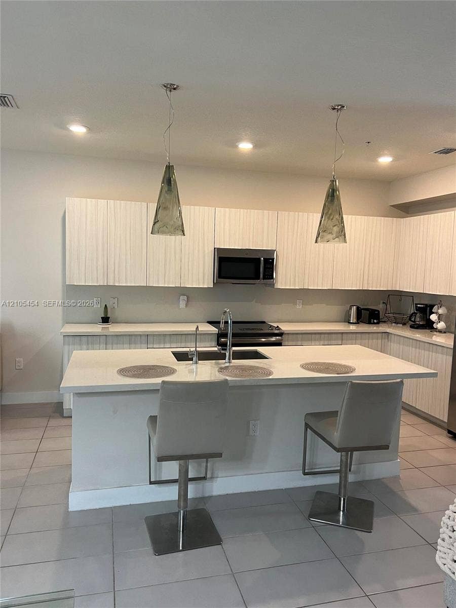 4745 NW 84th Court, #20, Doral, FL 33166 Modern kitchen featuring white cabinetry, a large kitchen island with integrated sink, recessed lighting, and two pendant light fixtures