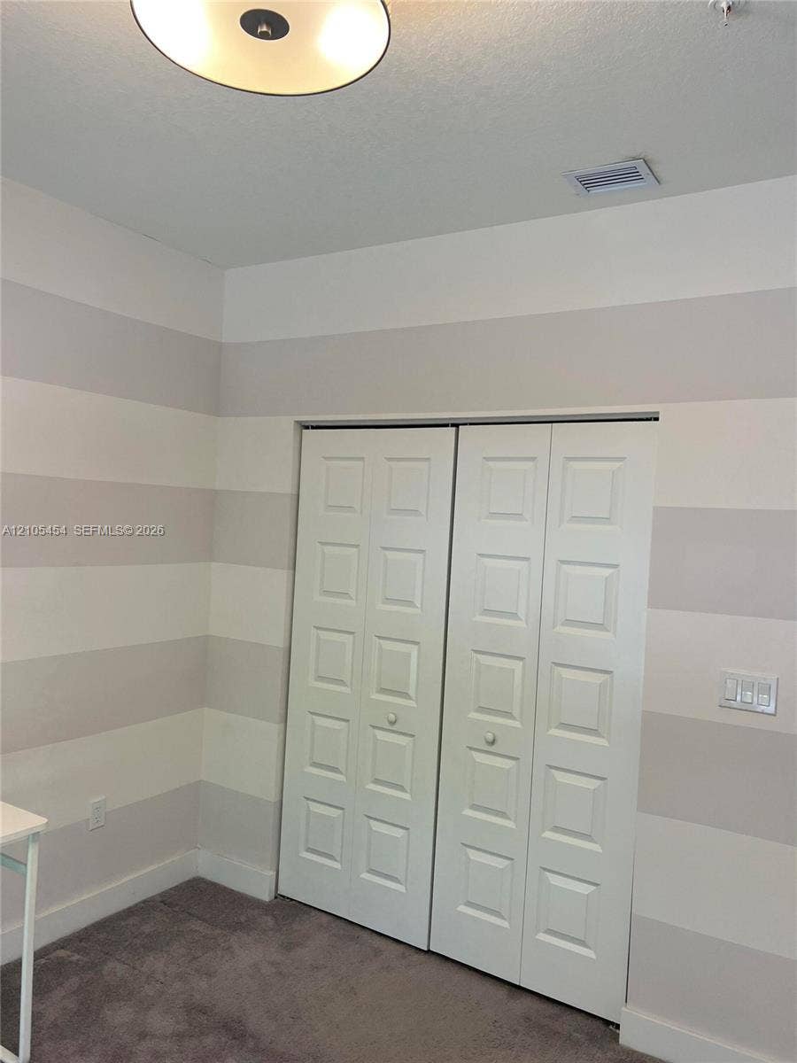 4745 NW 84th Court, #20, Doral, FL 33166 Recessed panel bifold closet doors, striped wall treatment, ceiling light fixture, and plush carpeting