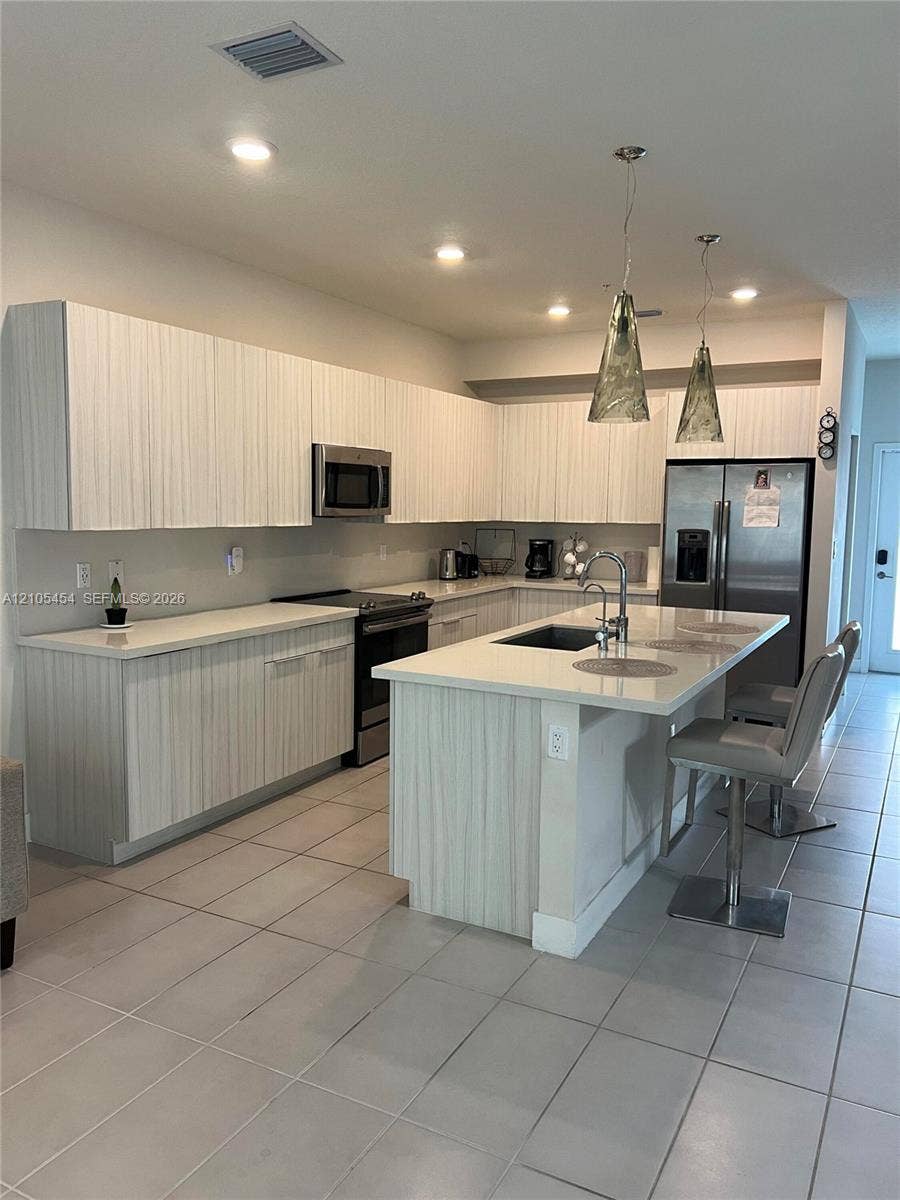 4745 NW 84th Court, #20, Doral, FL 33166 Kitchen featuring light wood-finish cabinetry, stainless steel appliances, a center island with sink, recessed lighting, and tile flooring