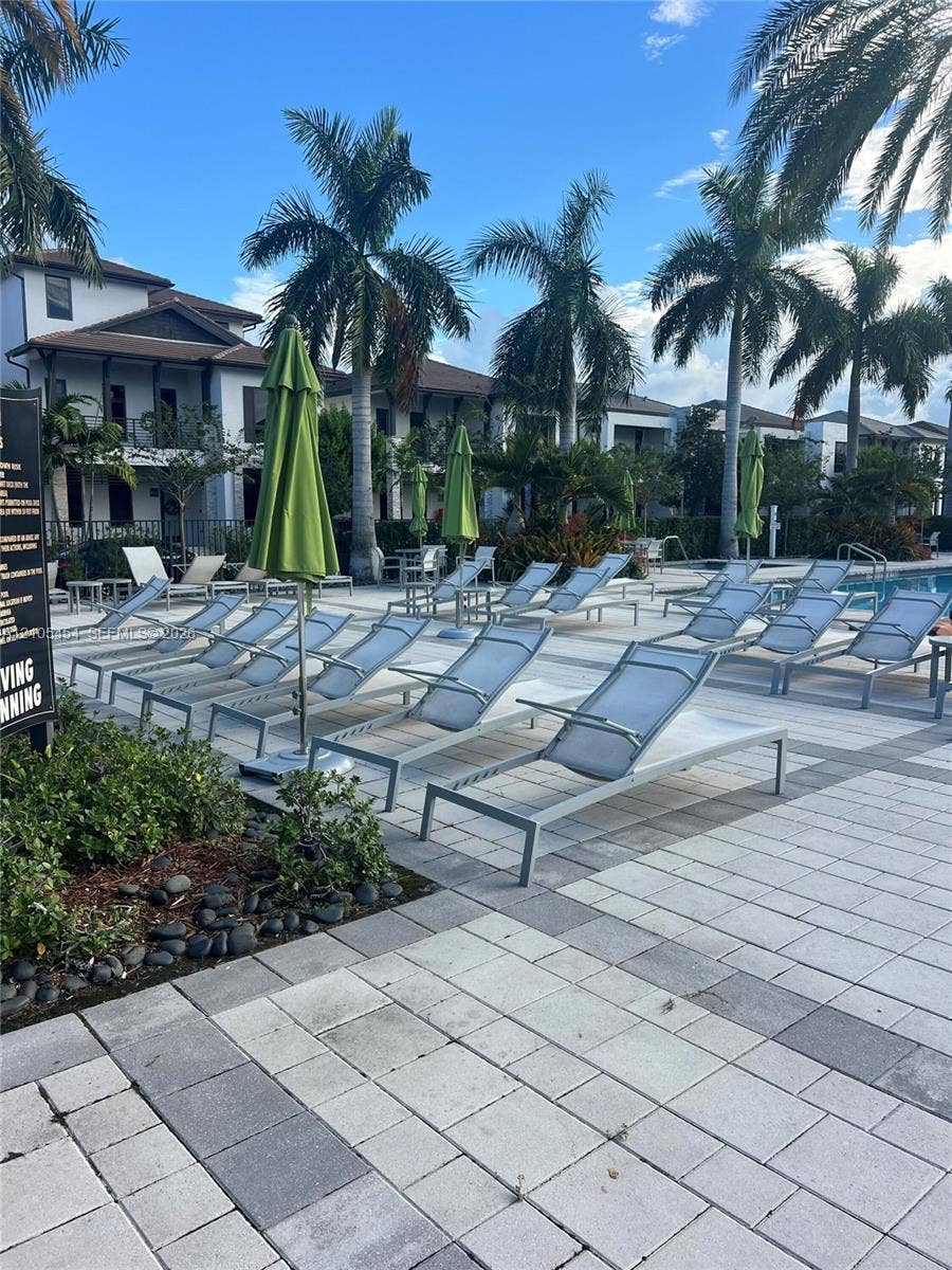 4745 NW 84th Court, #20, Doral, FL 33166 Expansive pool deck featuring paver flooring, multiple lounge chairs, and mature palm trees