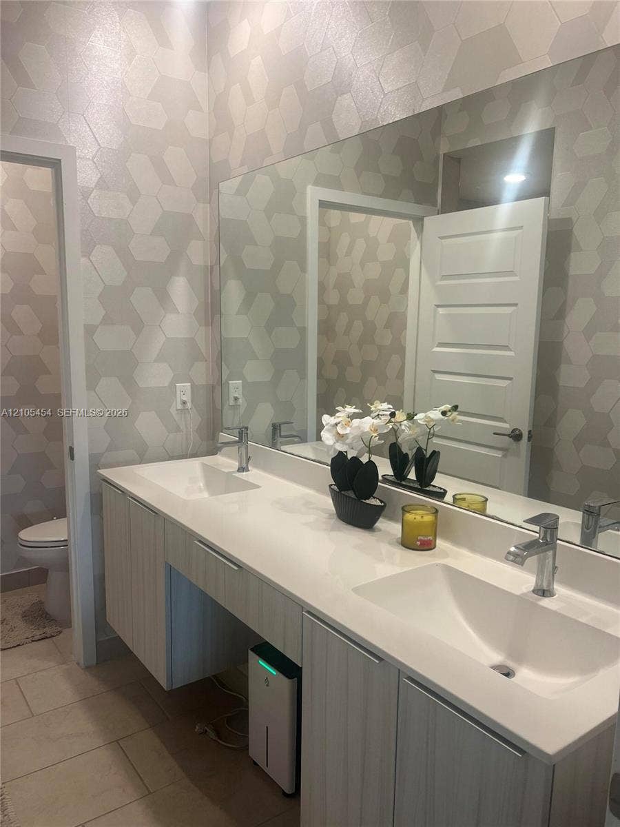4745 NW 84th Court, #20, Doral, FL 33166 Dual rectangular basin vanity with chrome faucets, a full-width mirror, and geometric pattern wall covering