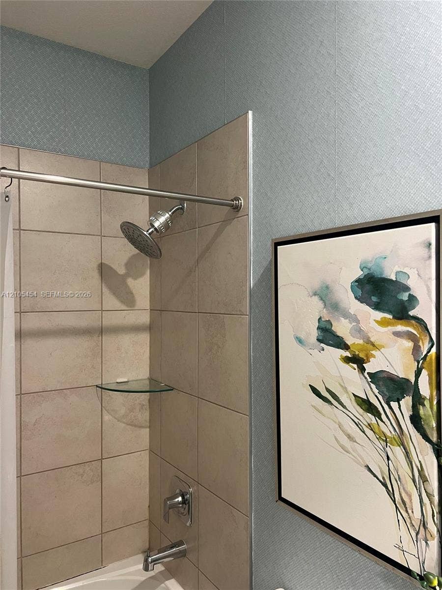 4745 NW 84th Court, #20, Doral, FL 33166 Bathtub with a tiled surround, a glass corner shelf, a brushed nickel showerhead, and a matching tub spout