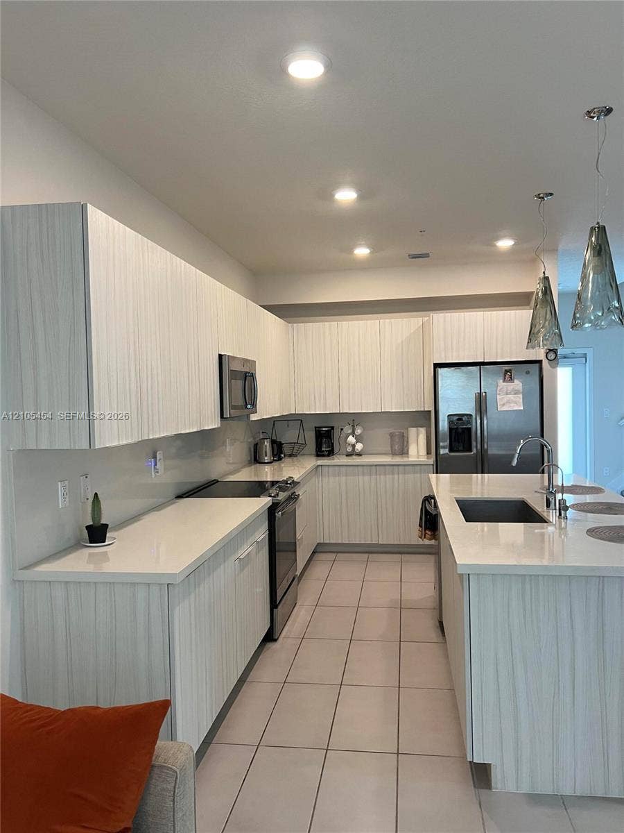 4745 NW 84th Court, #20, Doral, FL 33166 Contemporary kitchen featuring white cabinetry, light-toned countertops, stainless steel appliances, and an island with an integrated sink
