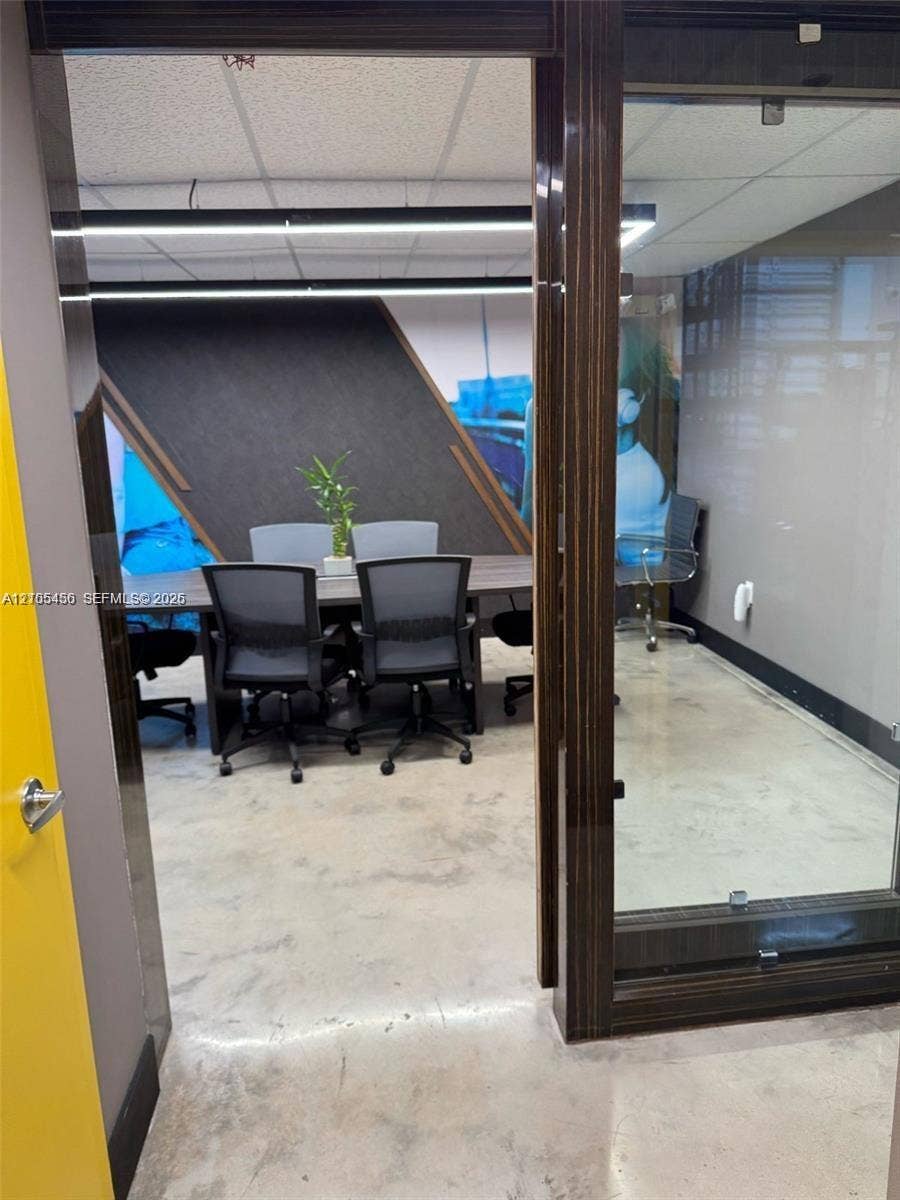 Concrete flooring, contemporary linear lighting fixtures, wood-finish door frames, glass partition, and acoustic paneling