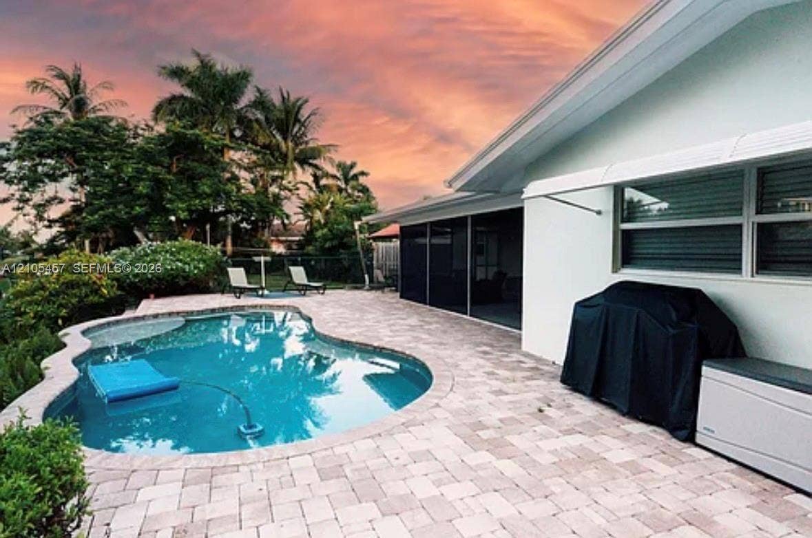 1083 SW 25th Avenue, Boynton Beach, FL 33426 Outdoor space featuring a paver patio, a freeform swimming pool, a screened-in lanai, and an exterior metal awning