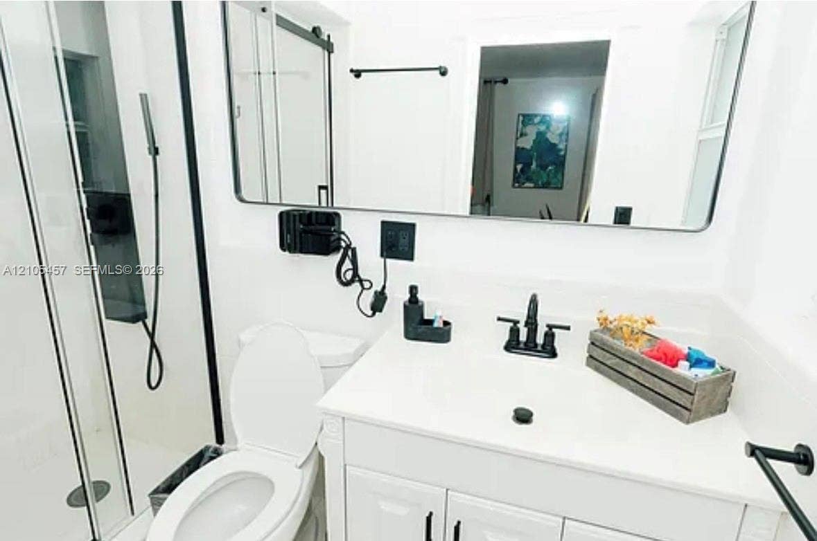 1083 SW 25th Avenue, Boynton Beach, FL 33426 Bathroom featuring a white vanity cabinet with a solid surface countertop, matte black widespread faucet, rectangular mirror with a black frame, and a walk-in shower with a matte black trim and hardware