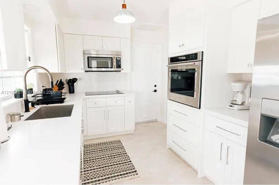 1083 SW 25th Avenue, Boynton Beach, FL 33426 Kitchen featuring white cabinetry, solid surface countertops, stainless steel wall oven, over-the-range microwave, and stainless steel undermount sink with a high-arch faucet