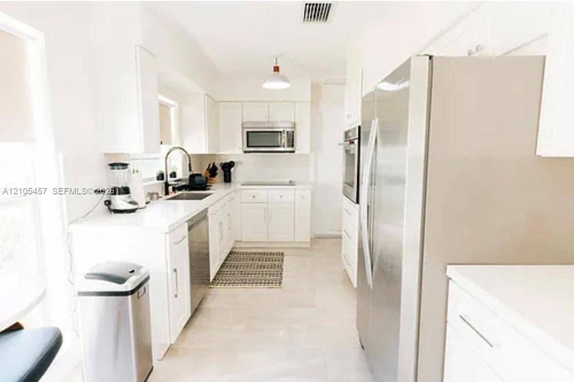 1083 SW 25th Avenue, Boynton Beach, FL 33426 Kitchen featuring white cabinetry, solid-surface countertops, stainless steel appliances, and a recessed sink with a high-arch pull-down faucet