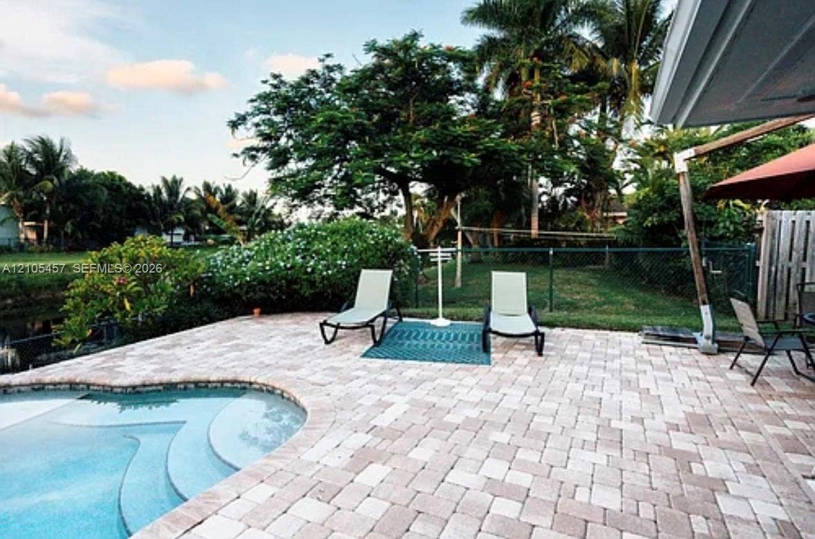 1083 SW 25th Avenue, Boynton Beach, FL 33426 Paver patio featuring a built-in swimming pool with rounded entry steps, perimeter chain-link fencing, and mature palm and shade trees