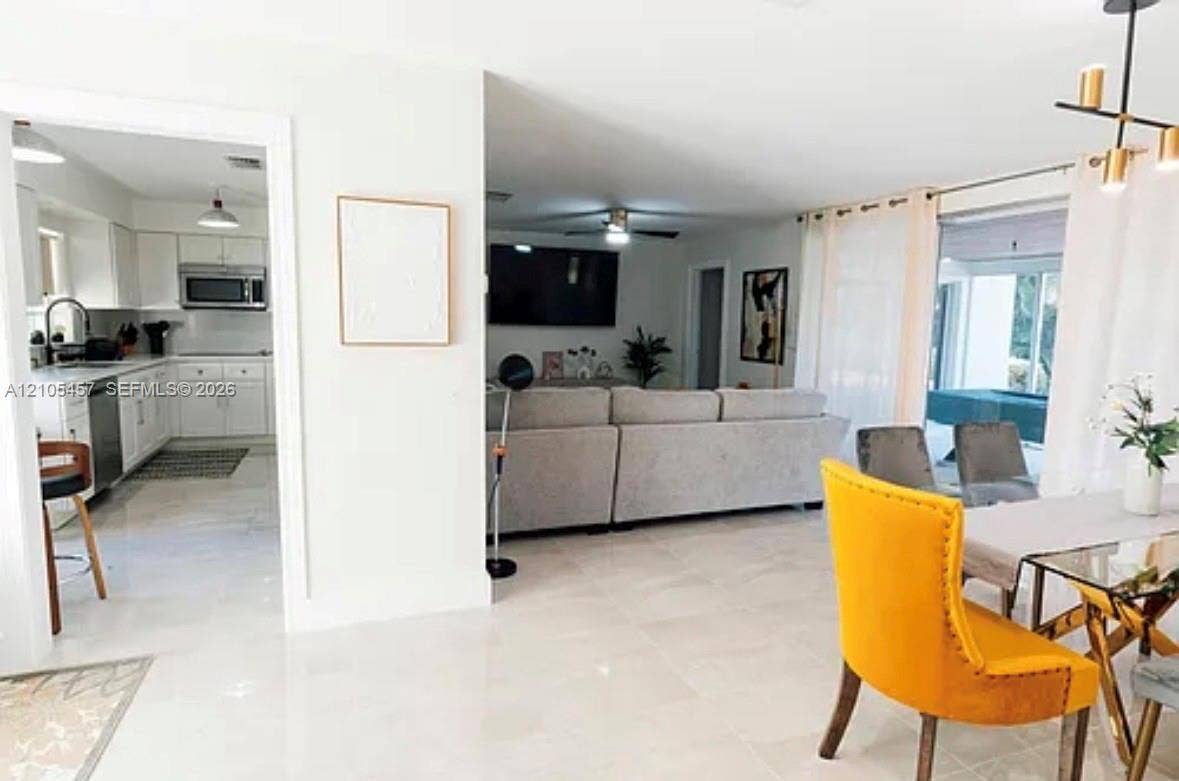 1083 SW 25th Avenue, Boynton Beach, FL 33426 Open-concept floor plan featuring large-format tile flooring, white cabinetry, integrated stainless steel appliances, and a modern multi-light chandelier