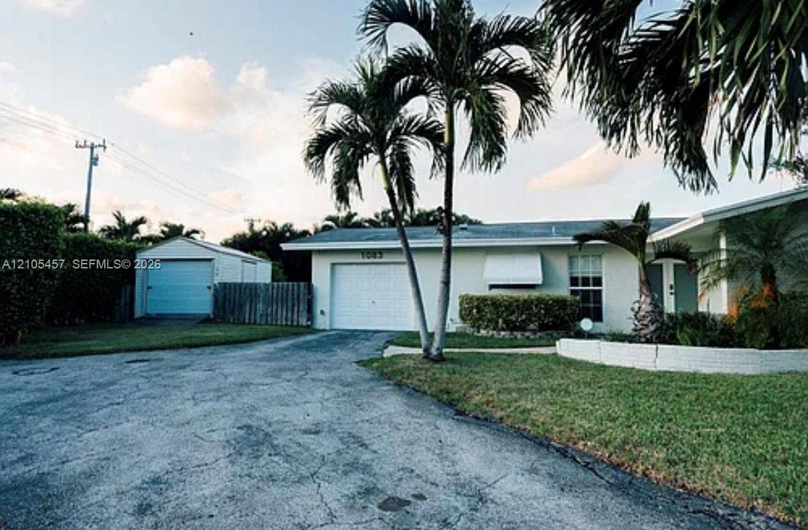 1083 SW 25th Avenue, Boynton Beach, FL 33426 Single-story exterior featuring a painted stucco facade, attached garage, detached storage structure, and low-profile concrete block retaining wall