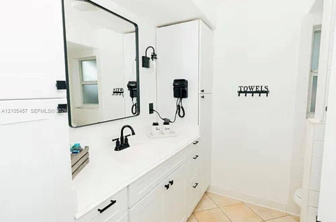 1083 SW 25th Avenue, Boynton Beach, FL 33426 White shaker-style cabinetry with matte black hardware, integrated tall storage, rectangular framed mirror, and dual-handle matte black faucet