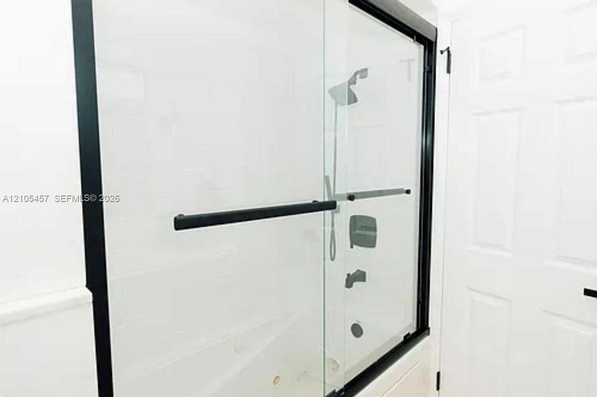 1083 SW 25th Avenue, Boynton Beach, FL 33426 Frameless glass shower enclosure with matte black hardware, integrated handheld showerhead, wall-mounted fixtures, and six-panel interior door