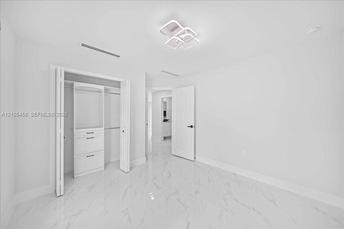 White tile flooring with subtle veining, modern ceiling light fixture, bi-fold closet doors, built-in closet organization with drawers, and a solid interior door