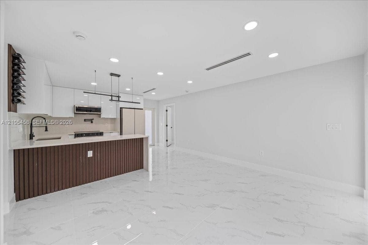 Kitchen island with vertical slat wood-finish paneling, white shaker-style cabinetry, a built-in wine rack, and a linear pendant light fixture