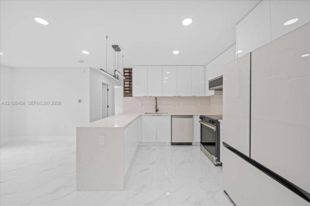 Sleek kitchen featuring white high-gloss cabinetry, stainless steel appliances, an expansive island, and recessed lighting