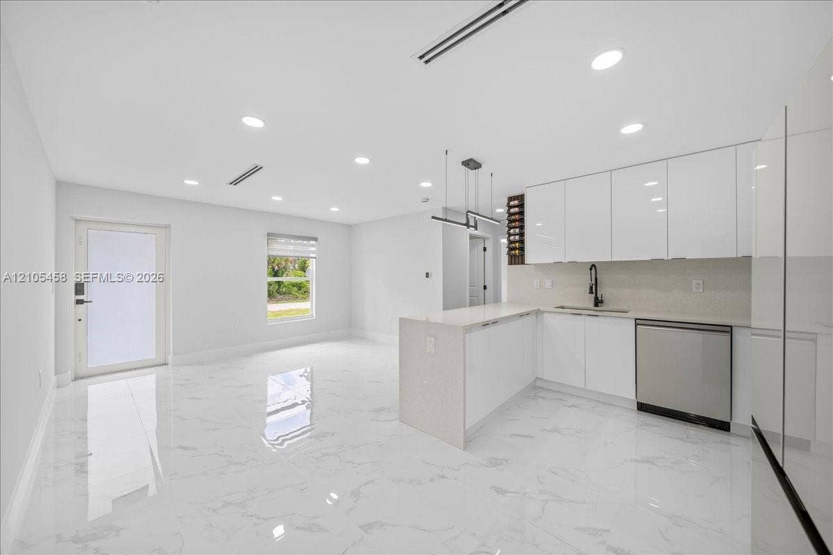 Open-concept layout featuring white high-gloss cabinetry, stainless steel dishwasher, integrated wine storage, white quartz countertops, and recessed lighting
