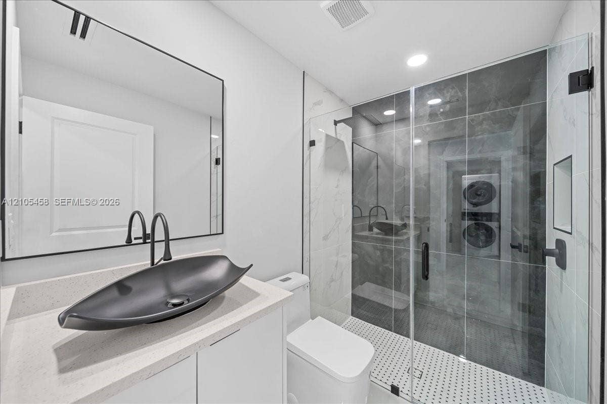 Modern bathroom featuring a glass-enclosed shower, vessel sink with matte black fixtures, white vanity cabinetry, and a light-toned countertop