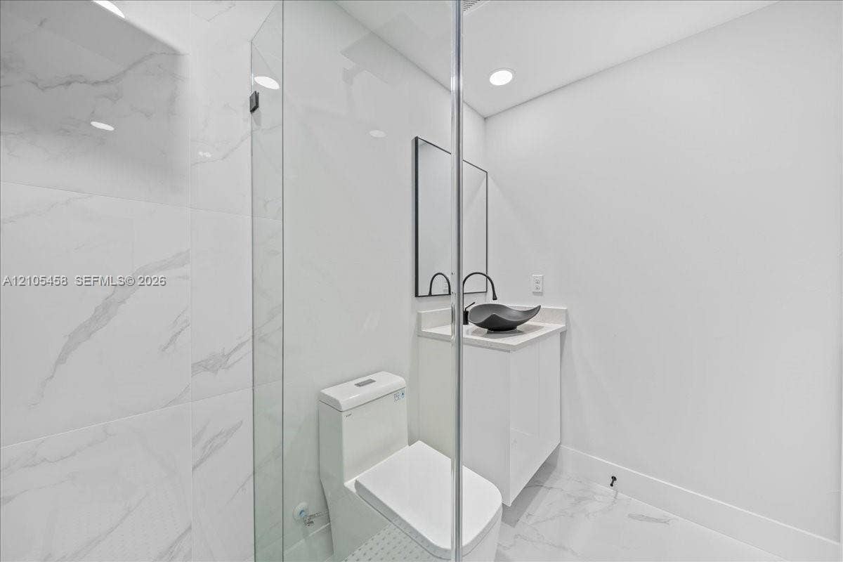 Glass-enclosed shower with large format tile surround, recessed lighting, modern vanity with vessel sink, and wall-mounted mirror