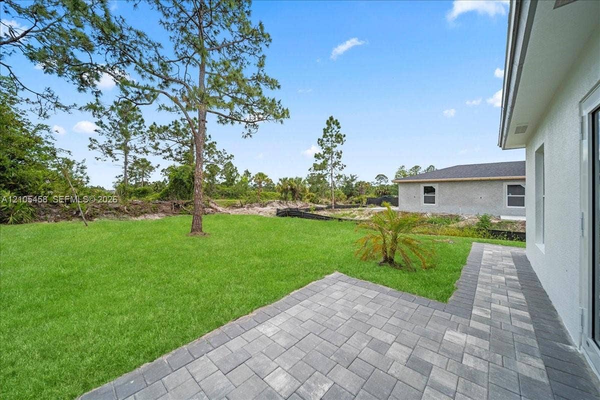Paved patio area, expansive lawn, mature tree, and exterior wall with windows