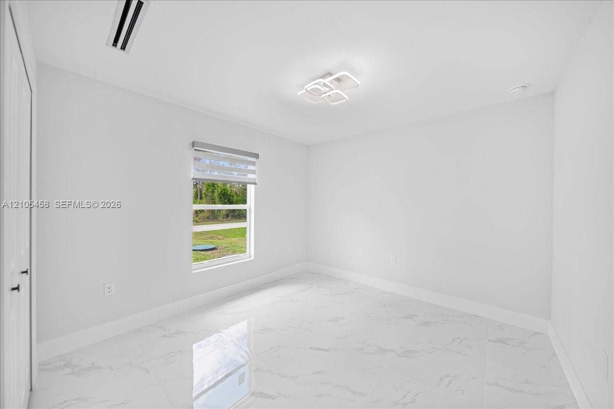 White tile flooring, modern ceiling light fixture, single window with blinds, white walls, and a white door with black hardware