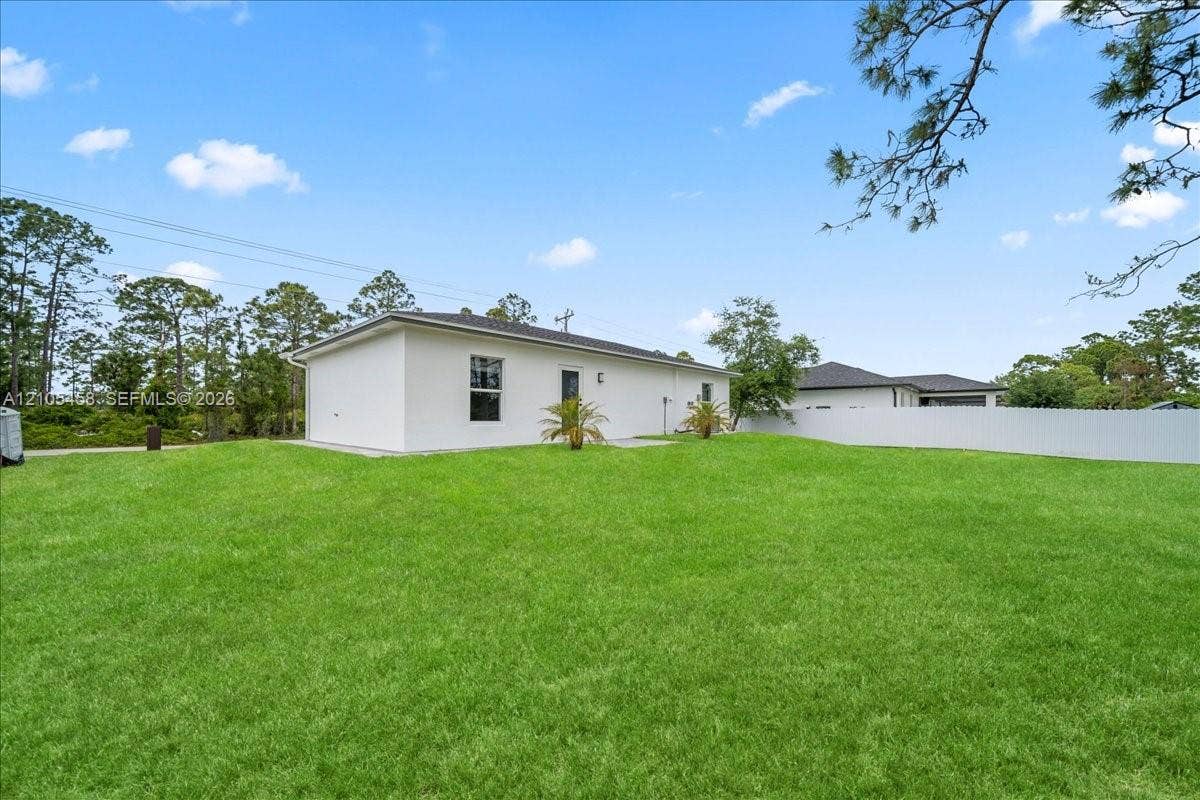 Expansive manicured lawn with mature landscaping and established trees, complemented by a modern white exterior featuring clean architectural lines and multiple windows