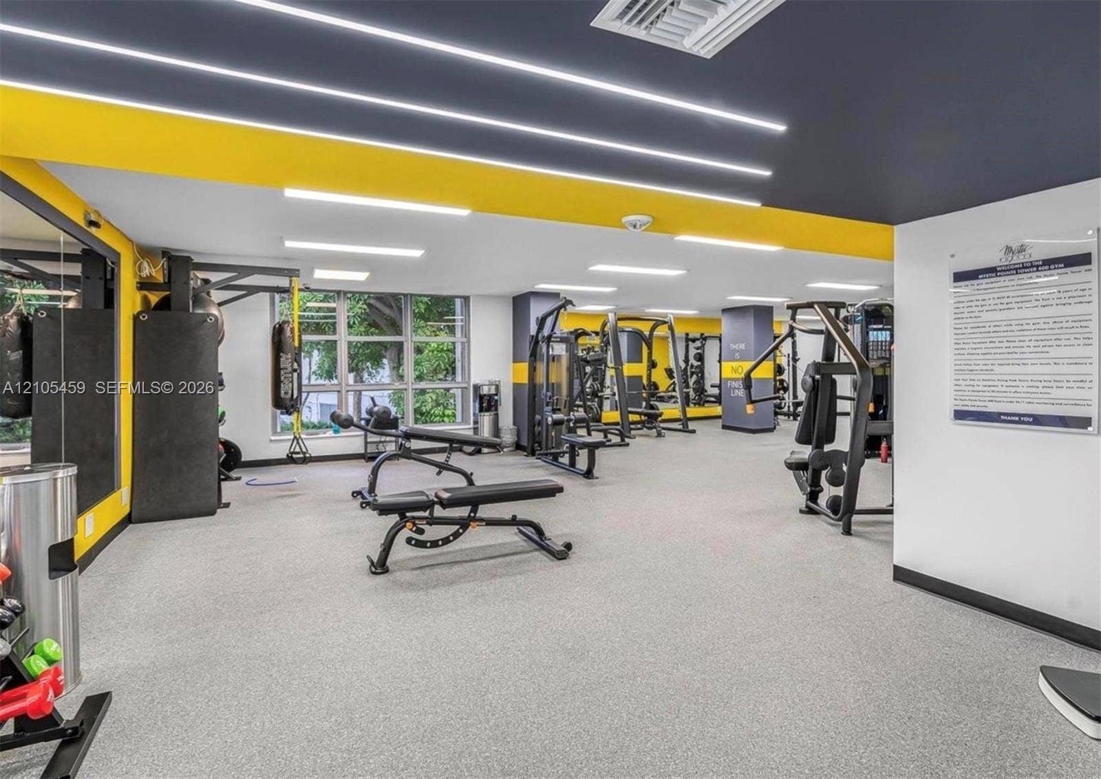 Fitness center with various exercise equipment, large windows, recessed linear lighting, and a durable flooring surface