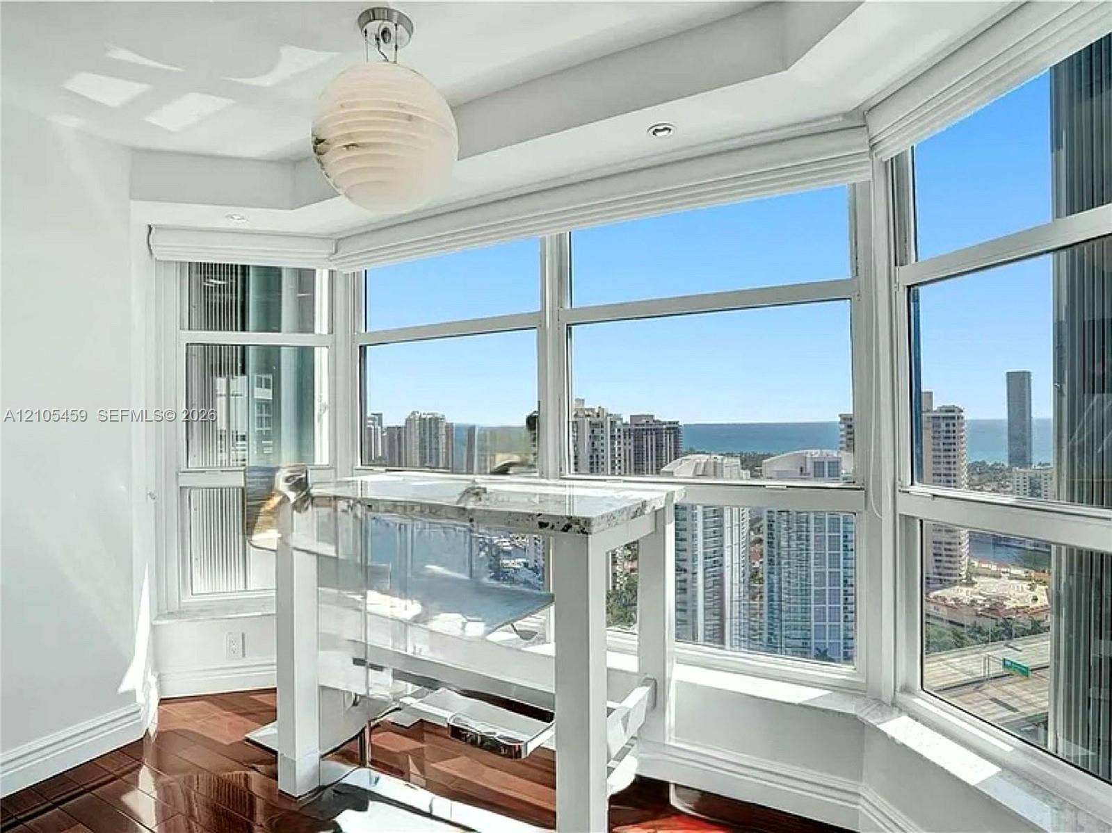 Bay window with expansive city and ocean scenery, complemented by wood-finish flooring and a spherical ceiling fixture