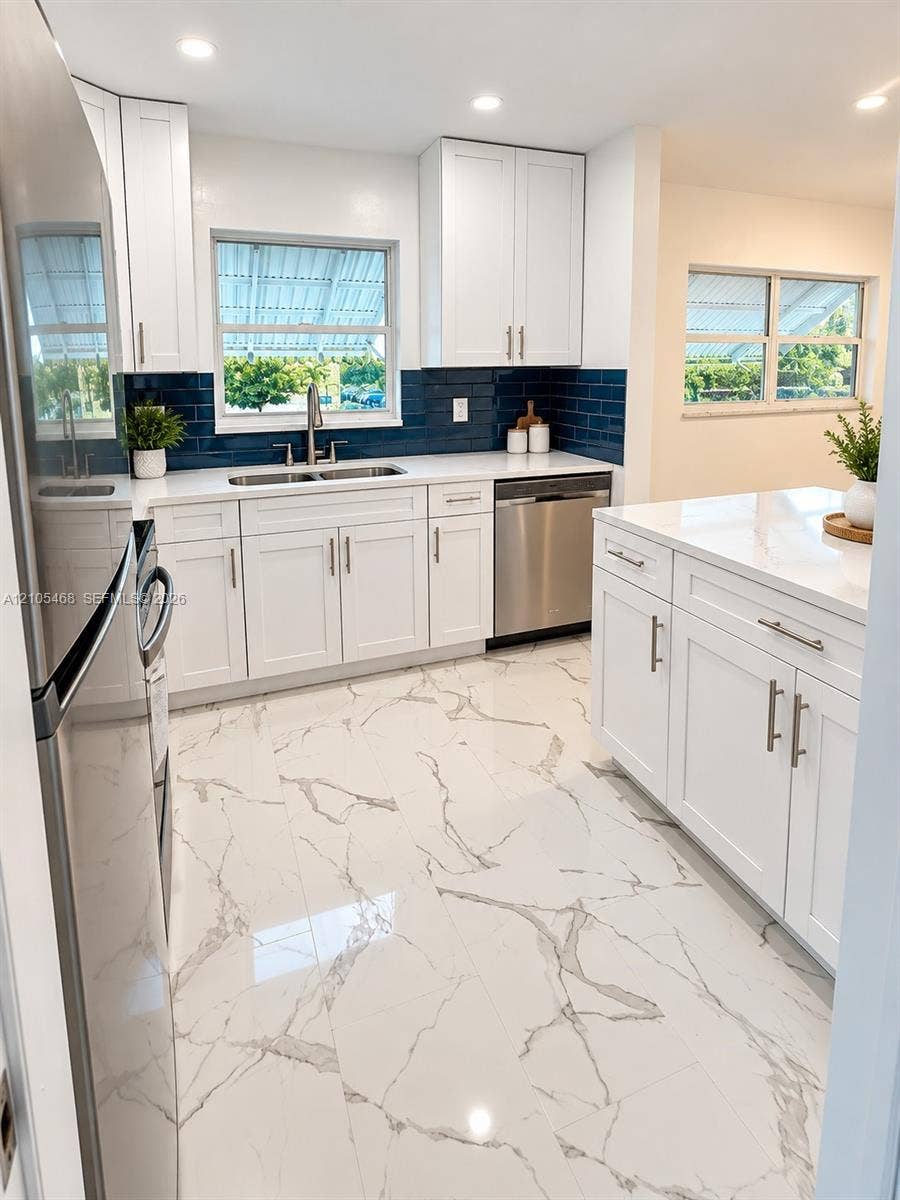 5300 Washington Street, #I201, Hollywood, FL 33021 Kitchen featuring white shaker-style cabinetry, a white countertop, a blue subway tile backsplash, stainless steel appliances, and large-format porcelain tile flooring