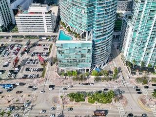 888 Biscayne Boulevard, #811, Miami, FL 33132 Contemporary high-rise building with a distinctive curved facade, featuring a rooftop amenity deck with an outdoor pool, surrounded by other urban structures and a street network