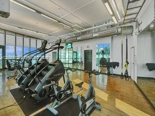 888 Biscayne Boulevard, #811, Miami, FL 33132 Expansive fitness area featuring floor-to-ceiling windows, wood-finish flooring, a full-length mirrored wall, and exposed ductwork