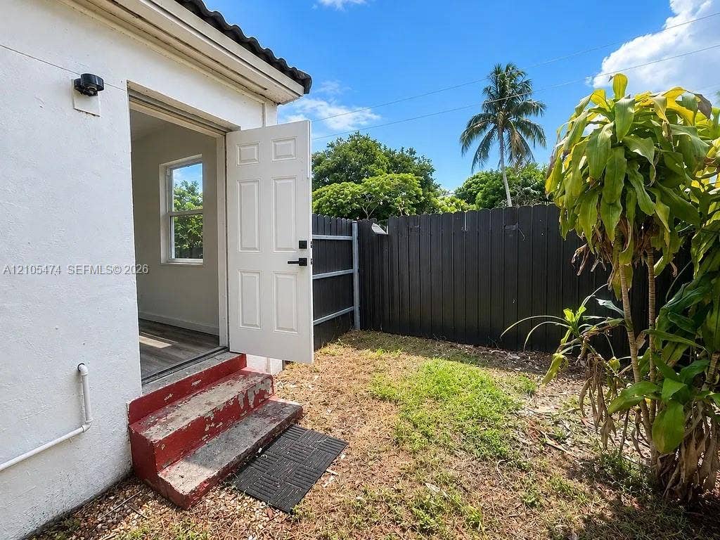 Picket fence with dark finish, exterior wall with stucco finish, single-panel door, window with single hung design, and wood-finish flooring