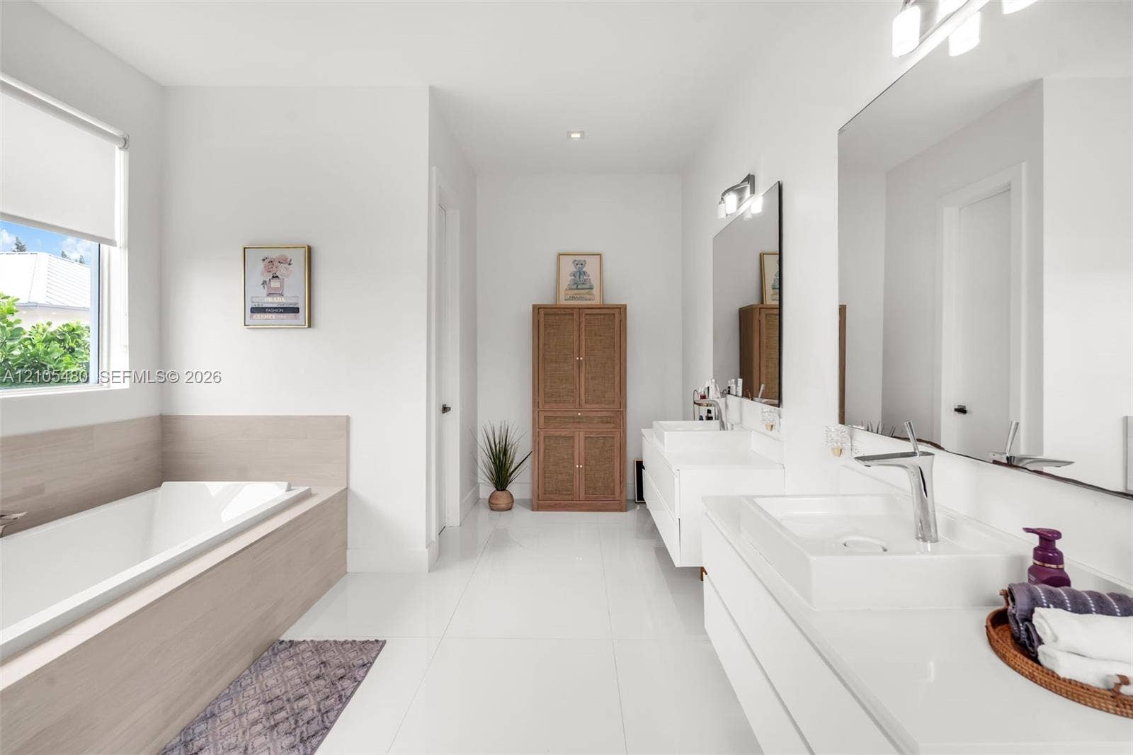 Integrated soaking tub with wood-finish surround, dual floating vanities with integrated rectangular sinks, extensive wall-mounted mirror, and tile flooring