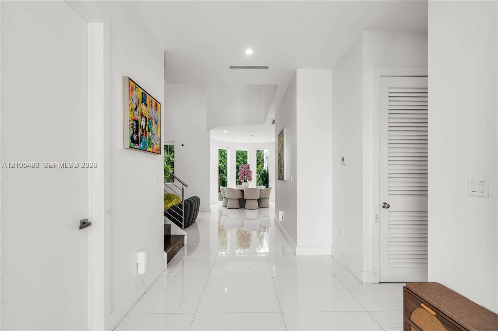 Expansive hallway featuring polished tile flooring, recessed lighting, white walls, a built-in staircase with a metal handrail, and a louvered door