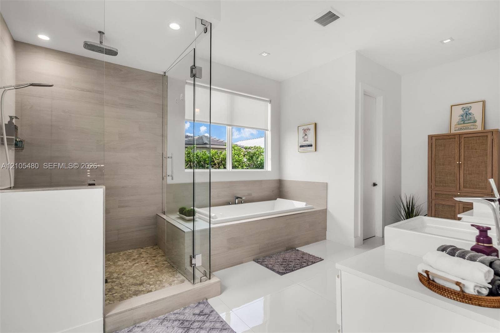 Spacious bathroom featuring a glass-enclosed shower with pebble flooring and a rainfall showerhead, a built-in bathtub, and recessed lighting