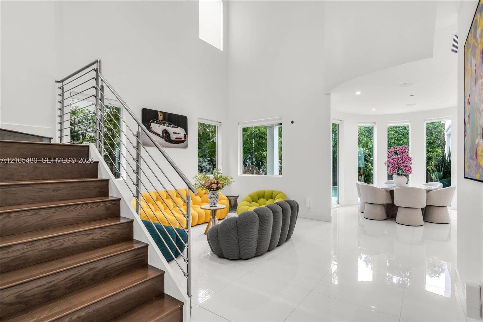 Two-story entry with wood-finish staircase, stainless steel railing, high ceilings, large format tile flooring, and multiple windows