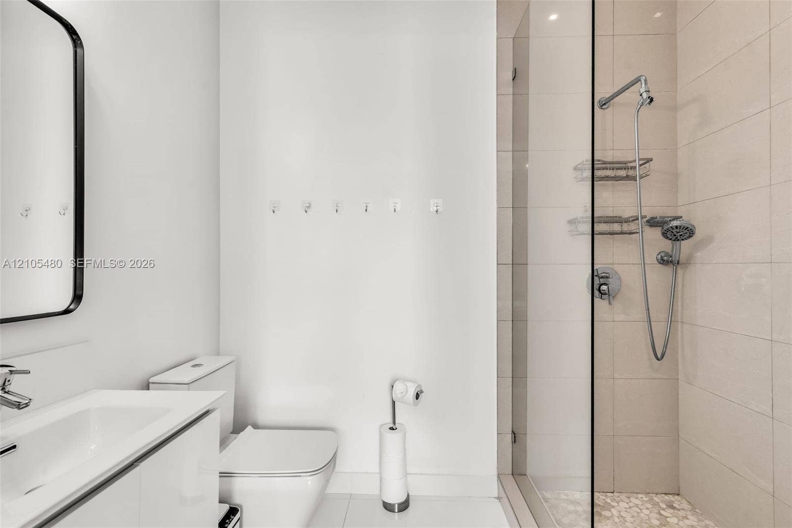 Modern vanity with integrated sink, sleek wall-mounted mirror, contemporary toilet, and a glass-enclosed shower with pebble-tiled flooring