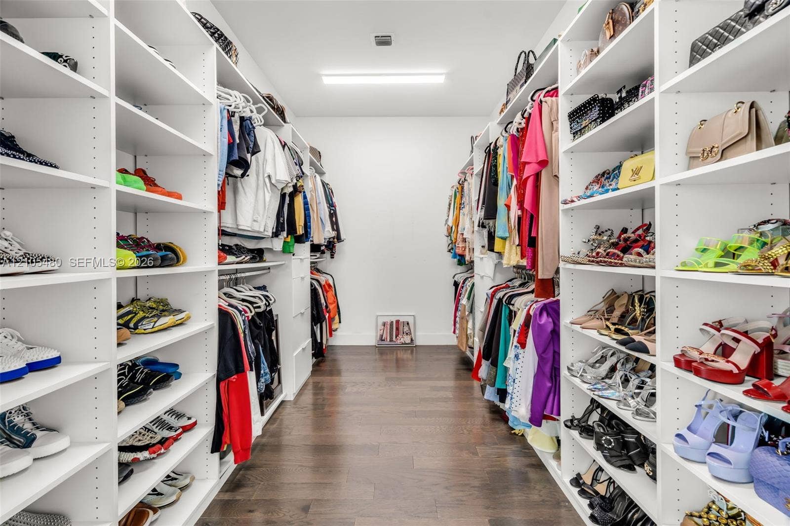 Walk-in closet featuring extensive built-in shelving, hanging rods, and wood-finish flooring
