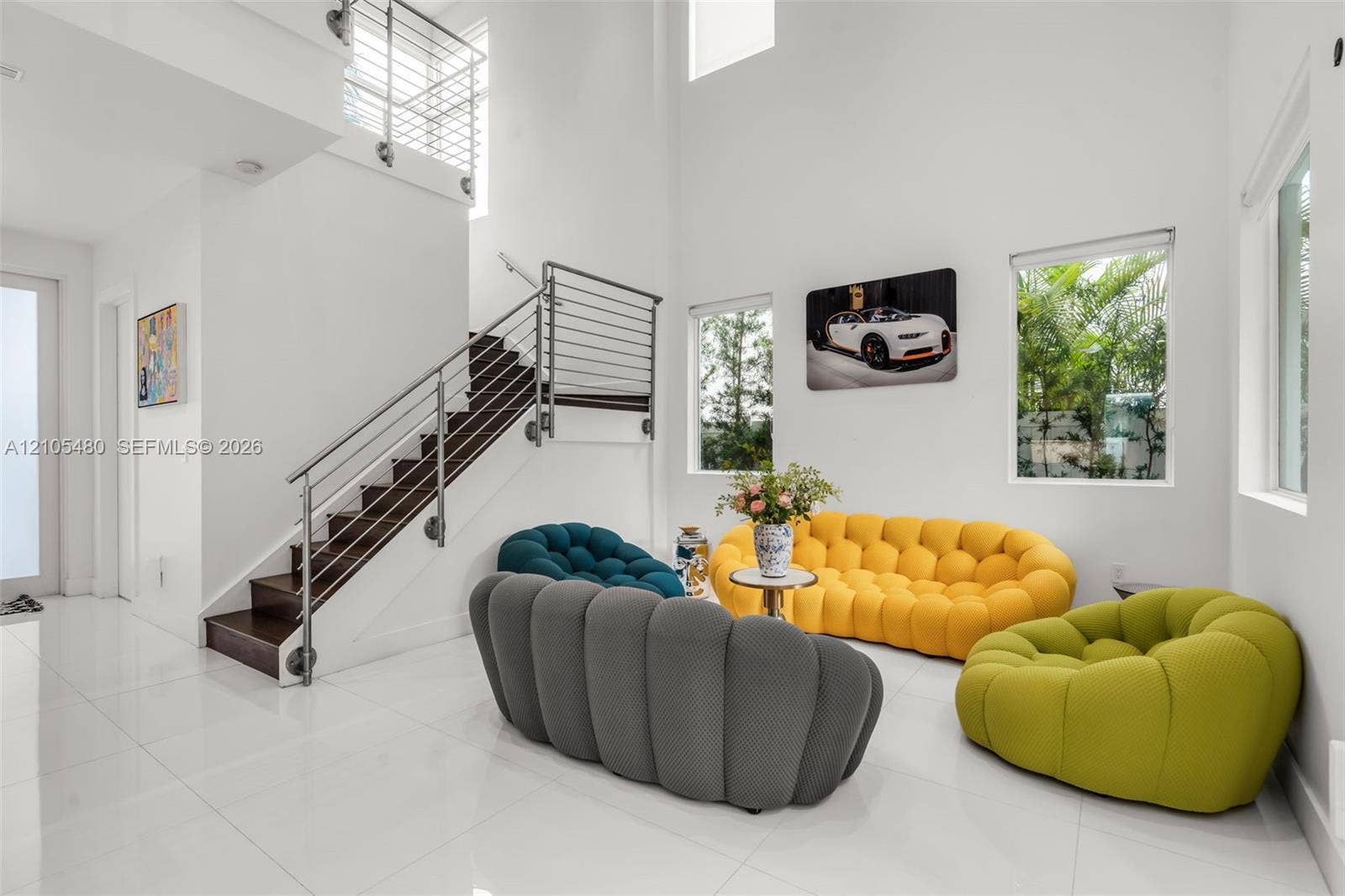 Soaring ceilings with upper windows, white tile flooring, dark wood-finish staircase, and stainless steel railings