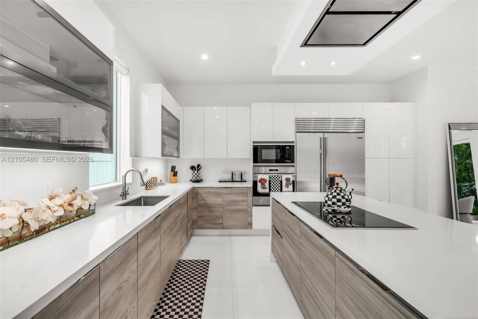 Modern kitchen featuring white glossy and wood-finish cabinetry, white countertops, stainless steel appliances, and an integrated cooktop on the island