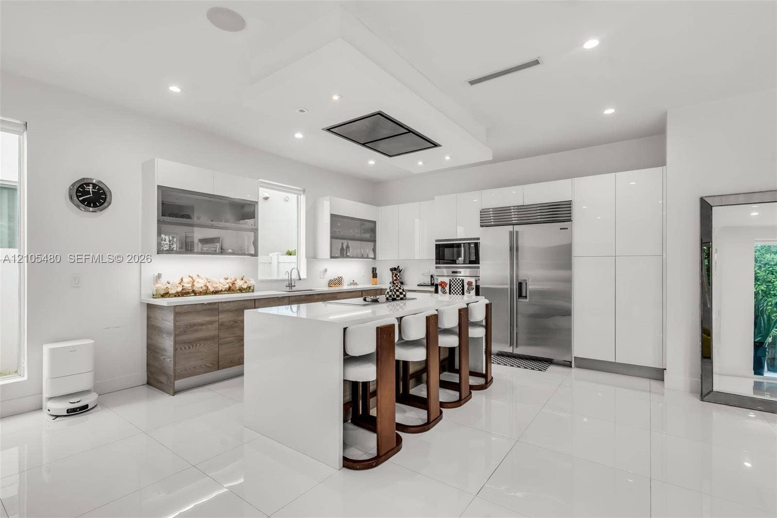 White gloss cabinetry, stainless steel appliances, central island with seating, white tile flooring, and recessed lighting