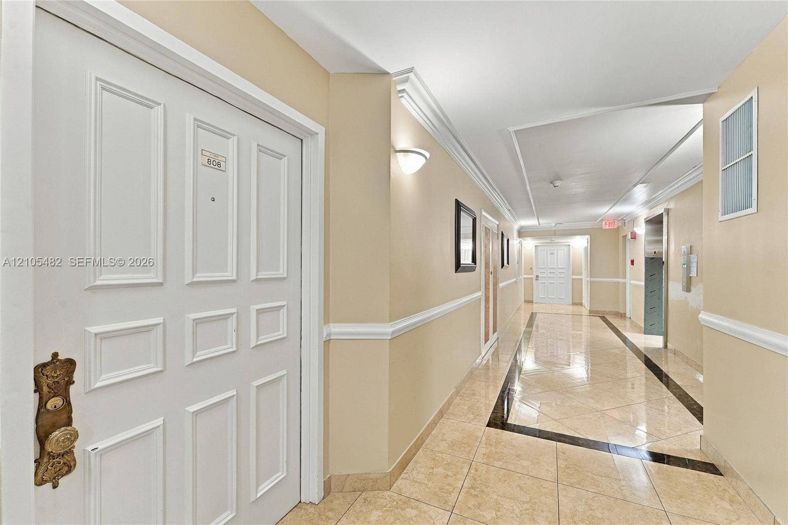 2100 S Ocean Lane, #808, Fort Lauderdale, FL 33316 Interior hallway featuring tile flooring with decorative dark inlay, wainscoting, crown molding, and wall-mounted sconce lighting