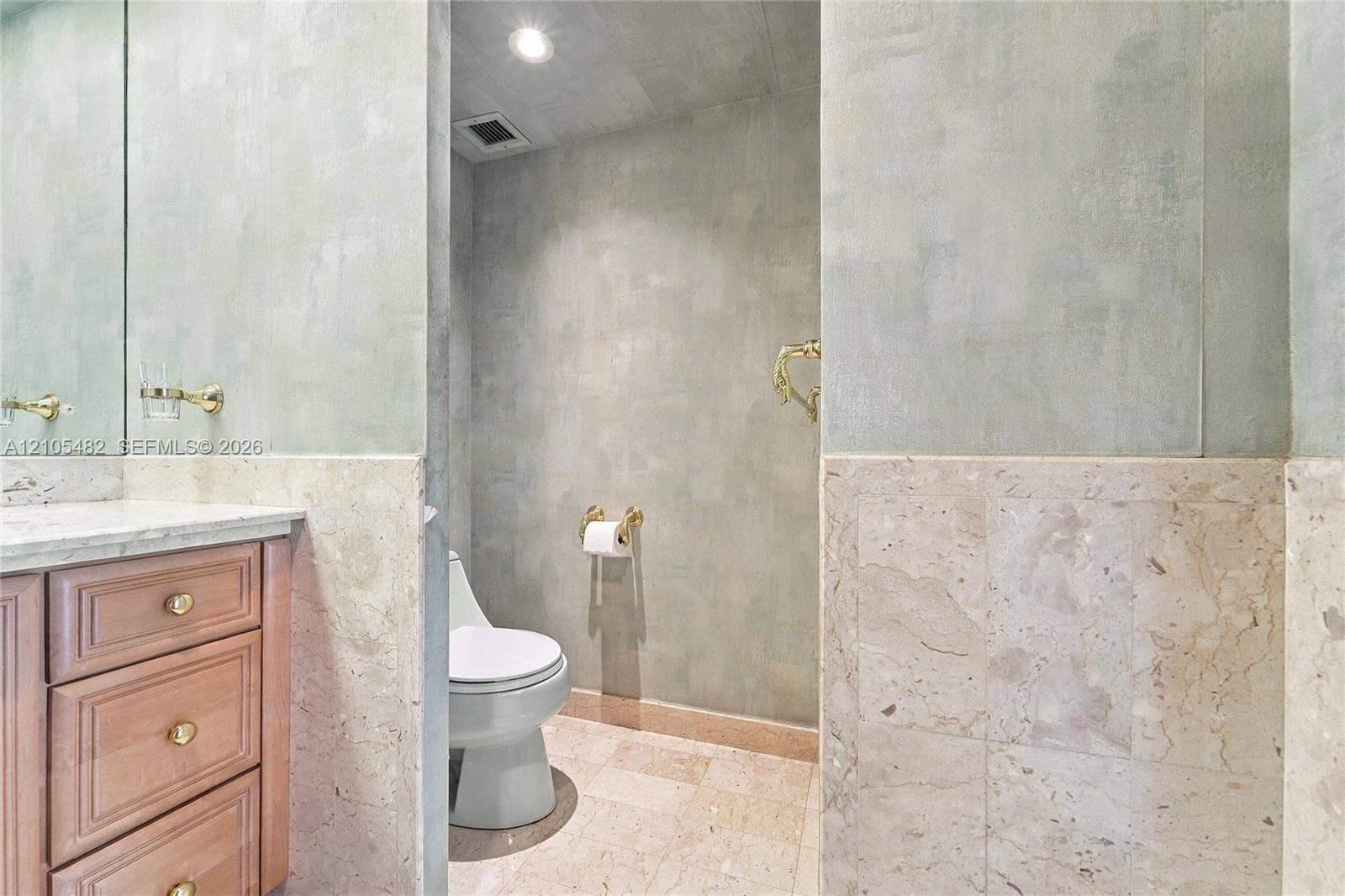 2100 S Ocean Lane, #808, Fort Lauderdale, FL 33316 Custom wood vanity with stone countertop, large-format mirror, brass-finish fixtures, and full-height stone tile wainscoting