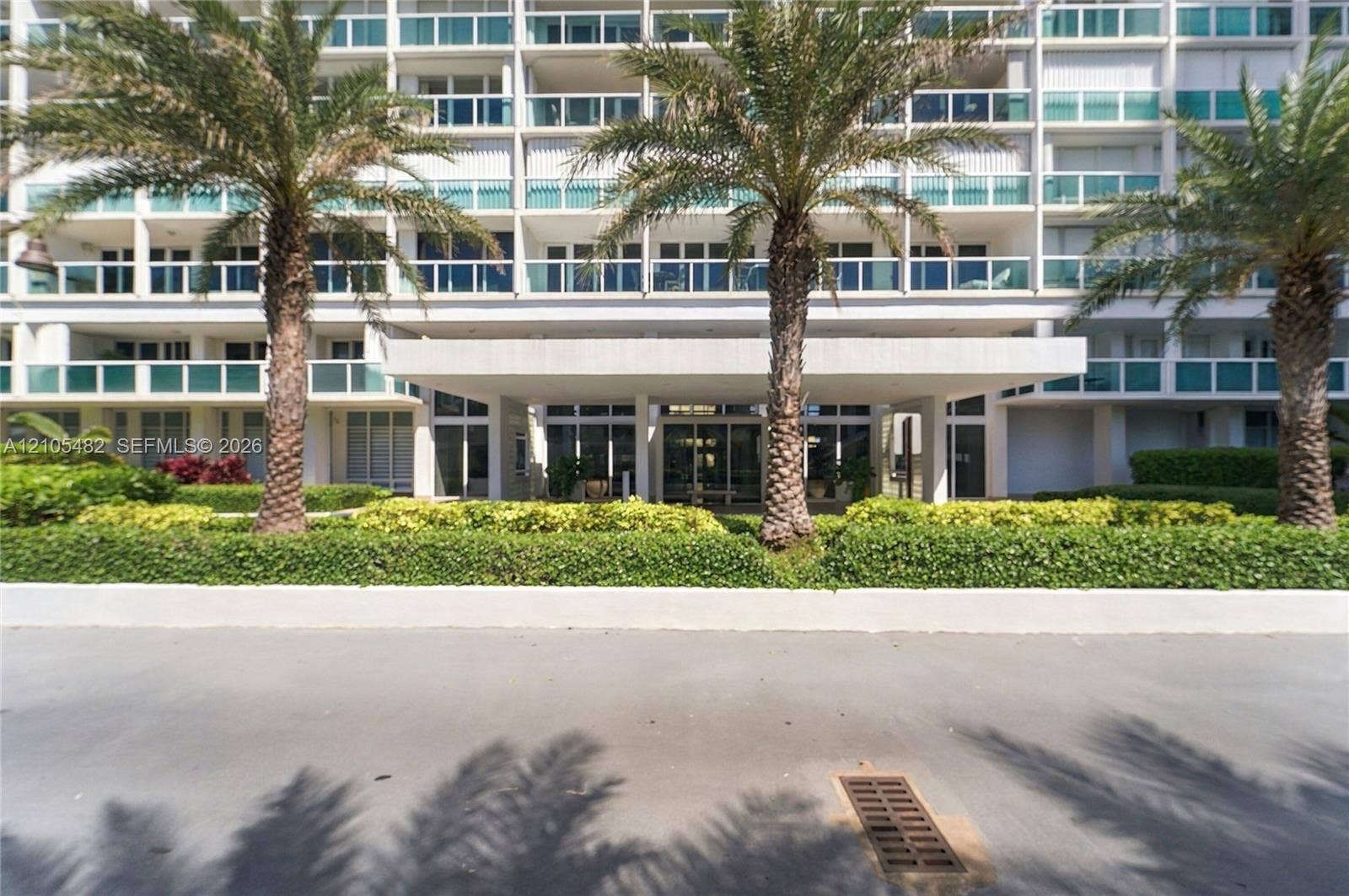 2100 S Ocean Lane, #808, Fort Lauderdale, FL 33316 Multi-story building exterior featuring a covered entryway, private balconies with glass railings, and manicured landscaping with palm trees