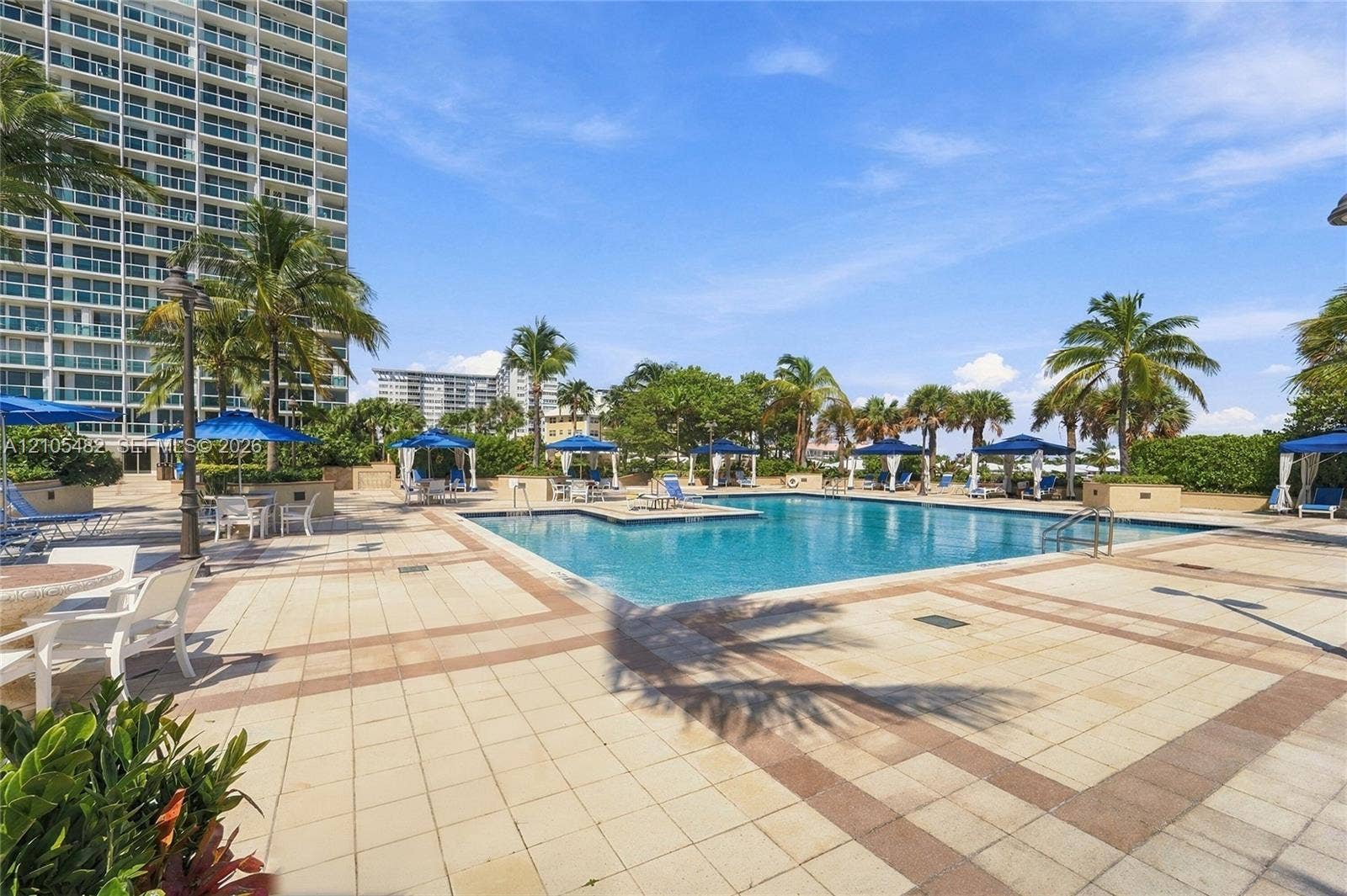 2100 S Ocean Lane, #808, Fort Lauderdale, FL 33316 Swimming pool with tiled decking, surrounding mature palm trees, and perimeter landscape hedging