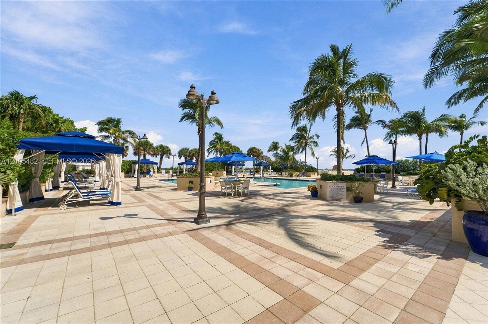 2100 S Ocean Lane, #808, Fort Lauderdale, FL 33316 Expansive pool deck featuring light-toned concrete pavers with brick-style accents, an in-ground swimming pool, decorative metal lighting posts, and mature palm trees